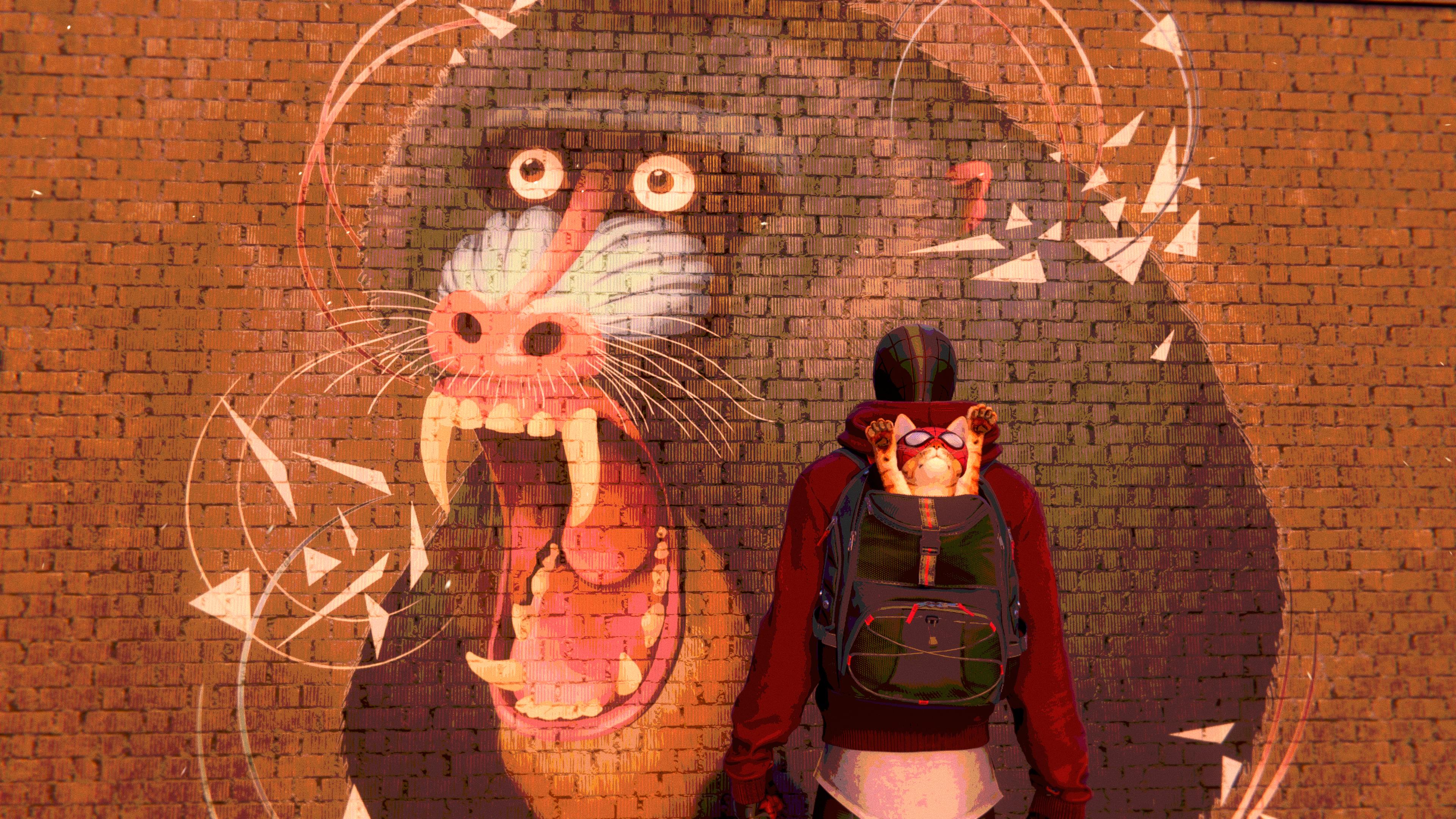 Miles Morales, in Spider-Man garb, with a backpack, out of which is emerging a cat in a mask, also named Spider-Man. They stand in front of a mural of a baboon baring its teeth.